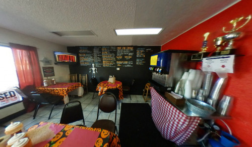 Few dining tables, a whole-wall chalkboard menu & a beverage dispenser machine on a counter, inside a tiny barbeque restaurant - Jessie Rae's BBQ serving Las Vegas style barbeque with homemade sauce