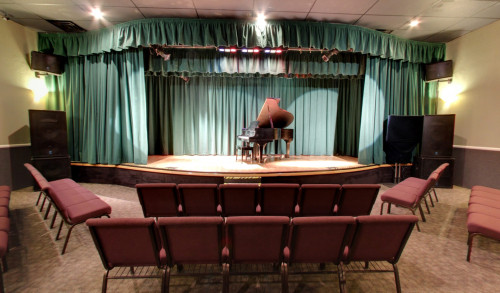 A piano at the center of a small theater stage, with cushioned seats in front, inside Family Music Center in Summerlin, Las Vegas