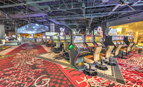 Multiple gaming machines aligned in a row in the casino area of SLS Las Vegas Hotel, with leather covered seats and fully carpeted floor.