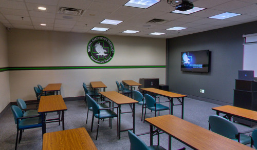 Multiple study chairs & tables facing a small monitor mounted on the wall inside one of the classrooms in North American Rescue - Education & Training school in the Las Vegas Valley, NV