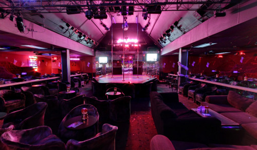A small stage with three dance poles, surrounded with cushy seats in a fully nude strip club - Little Darlings Las Vegas