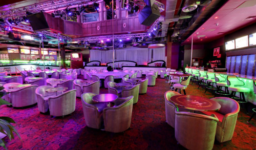 Bright neon lights & lots of small, round center tables paired with cushioned seats, surrounding the dance poles inside Larry Flynt's Hustler Club - Las Vegas' top rated strip club