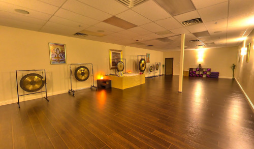 Six brass gongs aligned in a wide, warm-lit meditation room with wooden flooring in RYK Yoga and Meditation Center in Las Vegas