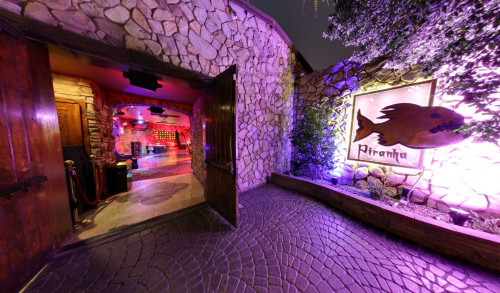 Las Vegas Piranha Nightclub - a lush gay nightclub in Vegas with its wooden doors opened showing the receiving area, next is their piranha logo placed on the bricked wall with backlight