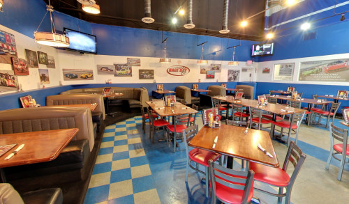 White & Blue racing track-themed interiors of Mo's Race Day Cafe in Speedway Blvd. Las Vegas, with its dining area filled with couches, wooden tables, metal chairs & race car photos on the wall