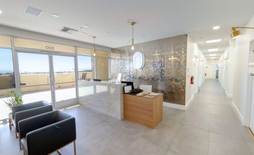 Bright ambiance of Novuskin Med Spa in Las Vegas, showing the receving area with it's front desk, an outside view through its transparent entrance doors & a right-side hallway towards the procedure rooms