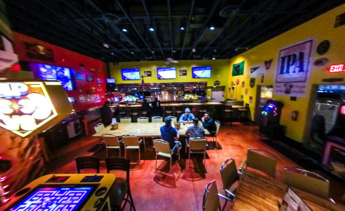 Arcade game machines are lined up along side the tables and chairs facing the bar area with brightly colored walls, inside Hi Scores Bar-Arcade in Las Vegas